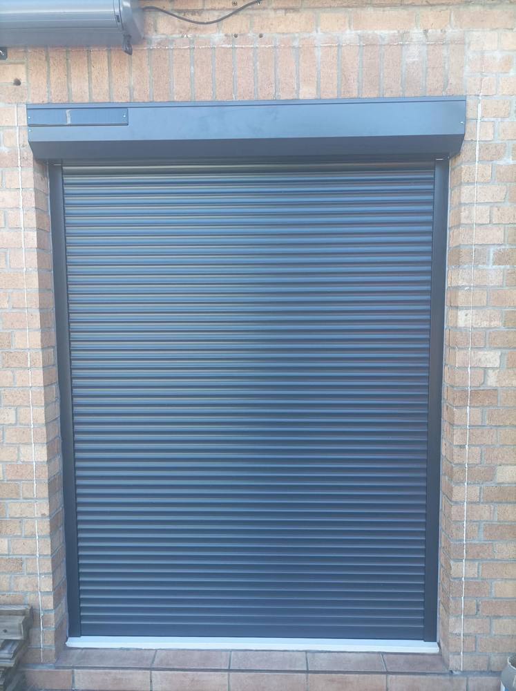 Volet roulant aluminium anthracite installé sur façade brique, coffre encastré